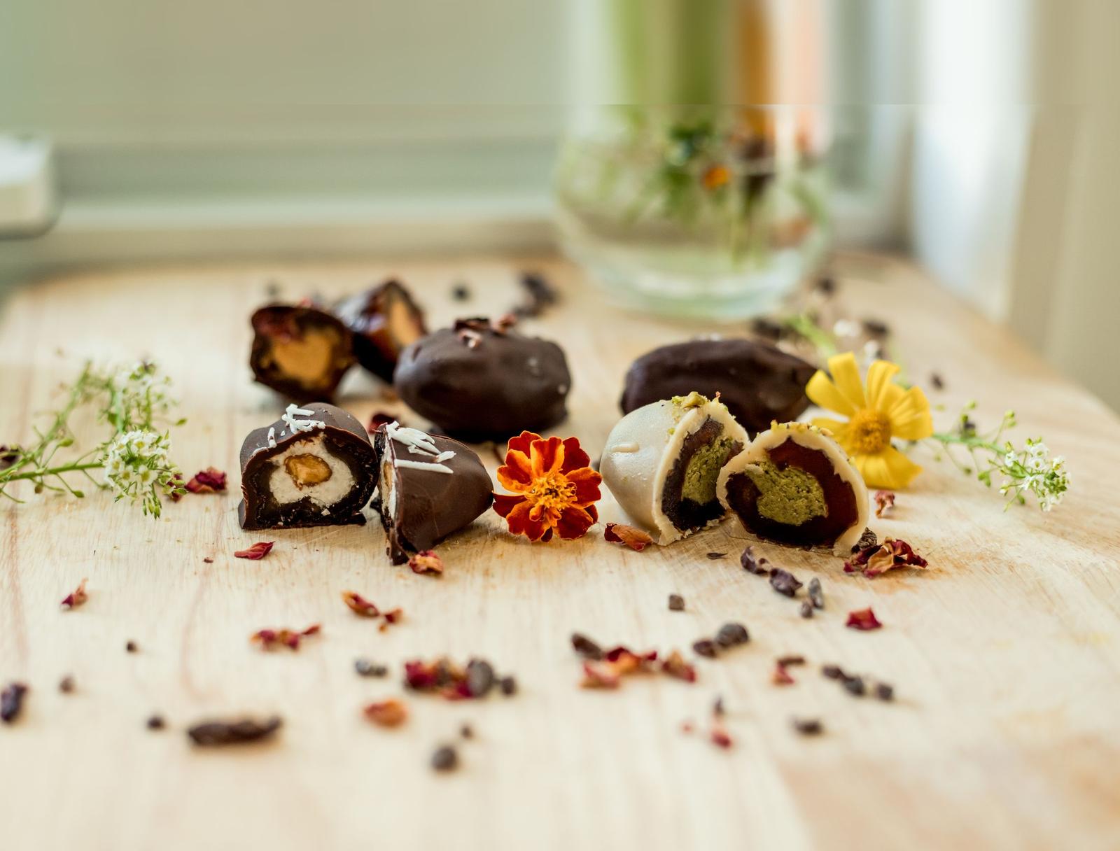 Flöra date bonbons cut in half on a wooden board with marigold, daisy and dried rose petals