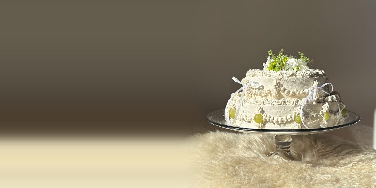 Two tier vintage Flöra cake with piped cream, green grapes and white ribbons, on a sheepskin in the sun