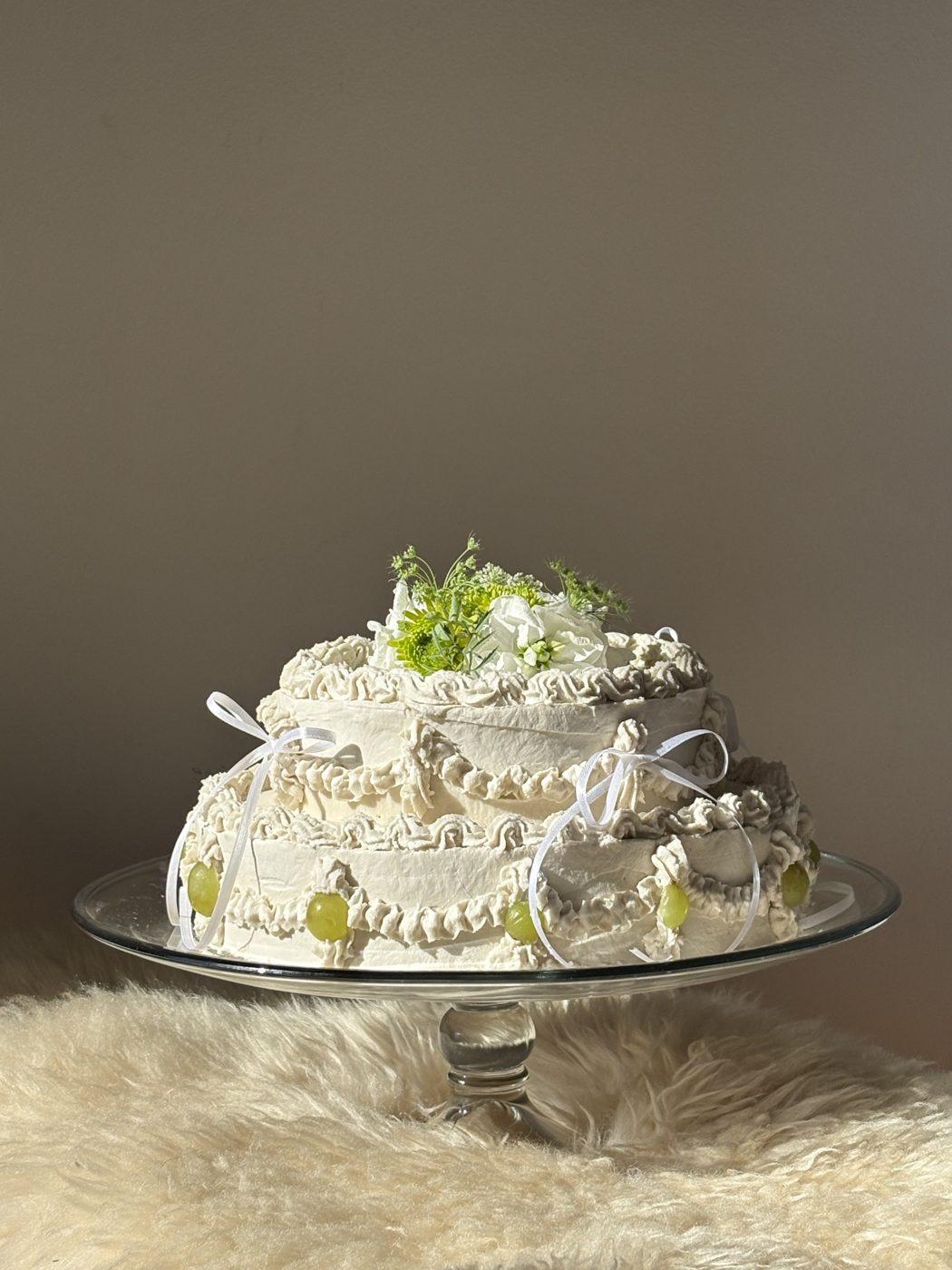 Two tier vintage Flöra cake with piped cream, green grapes, white ribbons and fresh flowers